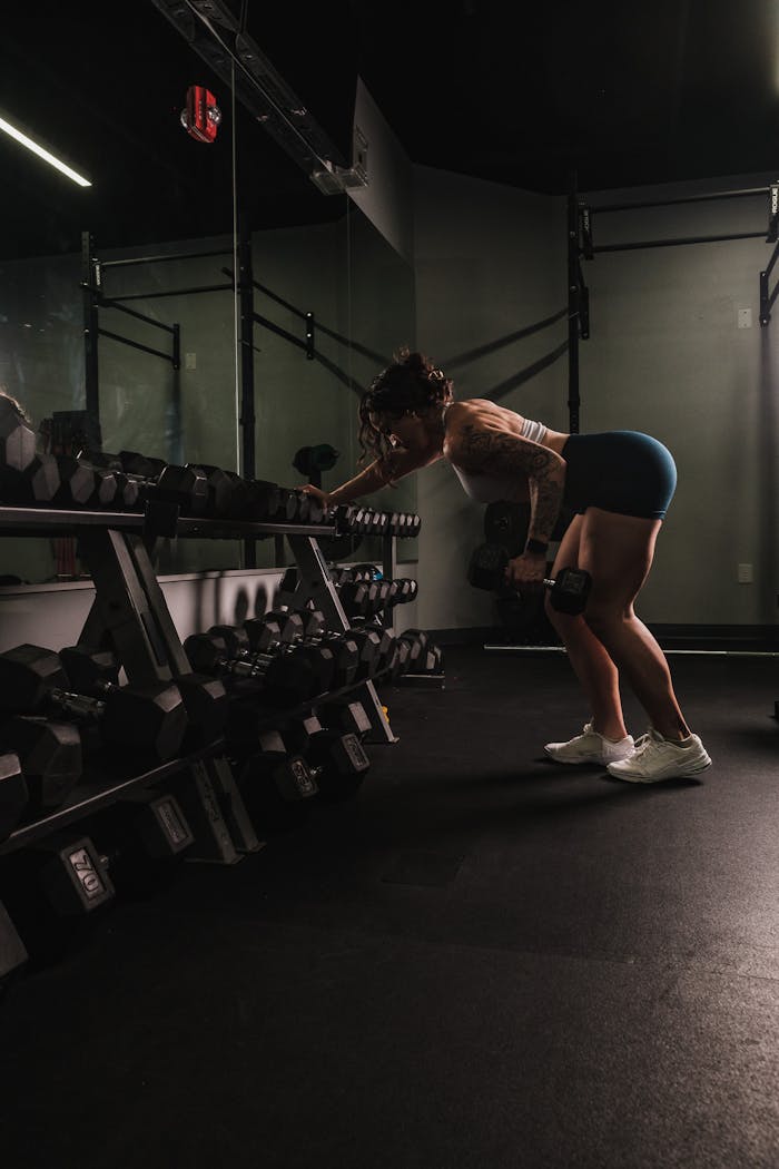 services-02 A woman performs a bent-over row with dumbbells in a gym, exemplifying strength and fitness.