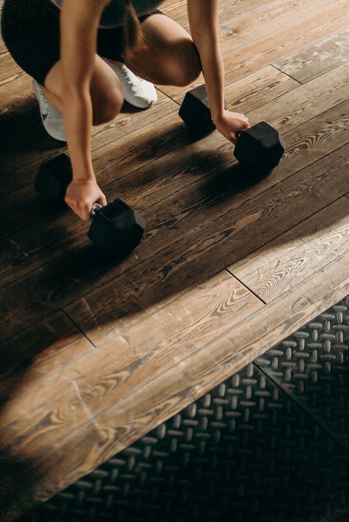 services-bg Female gym-goer in action with dumbbells on wooden floor, ready to lift.
